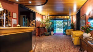 Un vestíbulo de hotel con un mostrador de recepción de madera, una alfombra estampada y una zona de estar con sillas amarillas.
