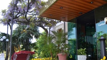 Ein Hotel Eingang mit einer hölzernen Markise, Sitzgelegenheiten im Freien sowie verschiedenen Pflanzen und Blumen.