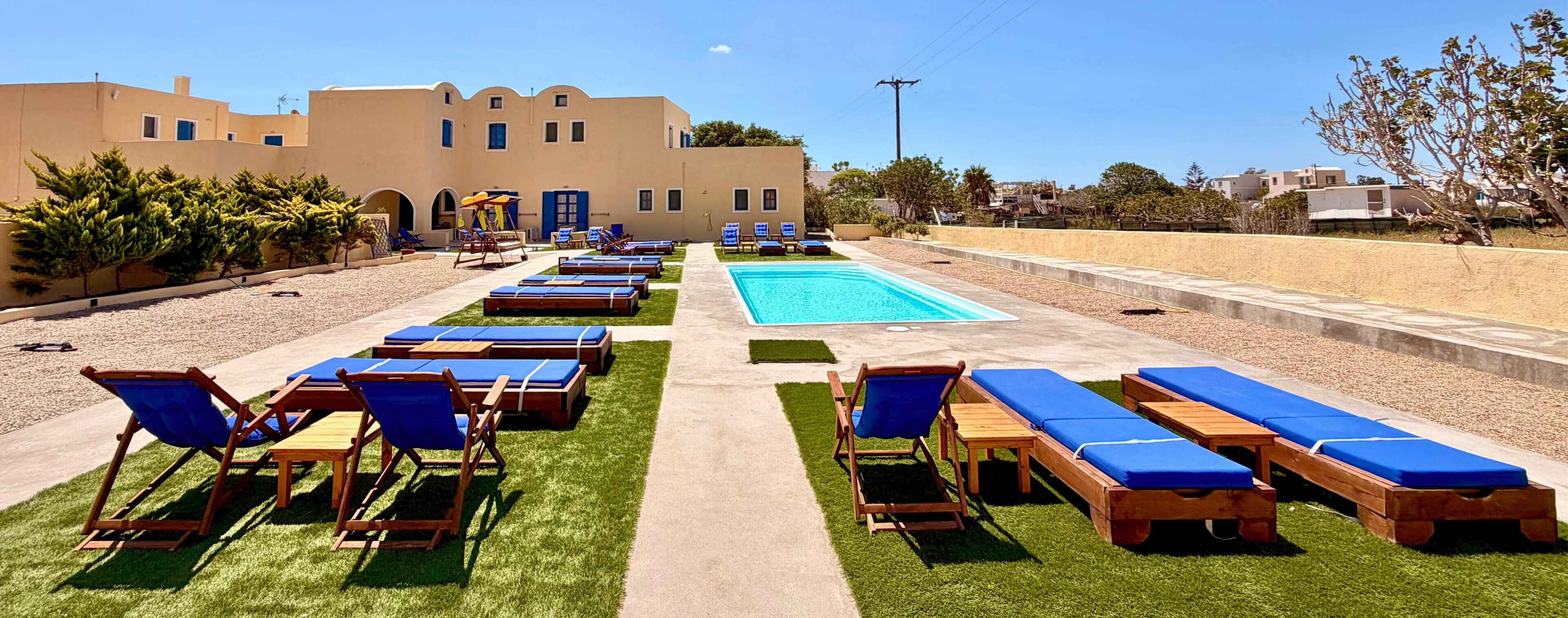 A poolside area with lounge chairs and a swimming pool, surrounded by a building with multiple windows and doors.