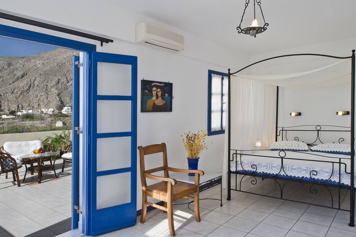 Un dormitorio con cama, una silla, una mesa y vistas a un paisaje montañoso.