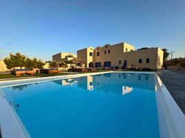 Una piscina con sillones de descanso y un edificio con varias ventanas y balcones.