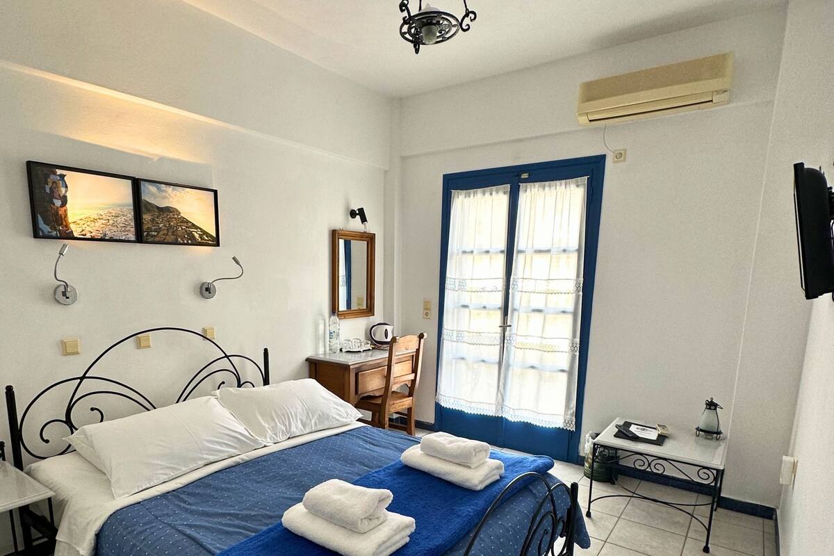 Un dormitorio con cama, escritorio, silla, ventana con cortinas y ventilador de techo.