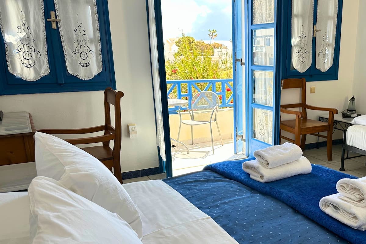 Habitación de hotel con cama, dos sillas, escritorio y balcón con vistas.