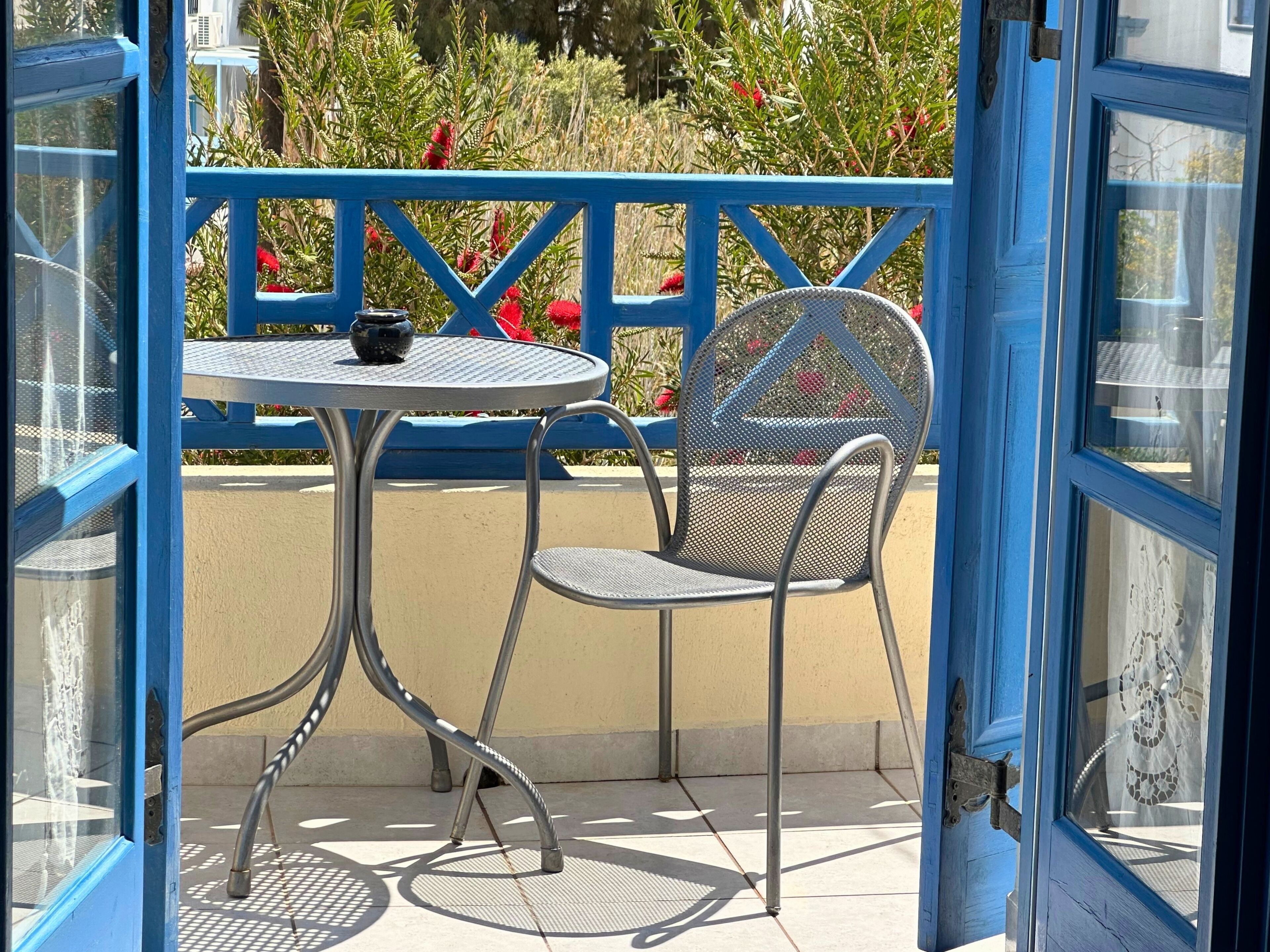 A blue-framed outdoor seating area with a round table and a chair, surrounded by a blue railing.