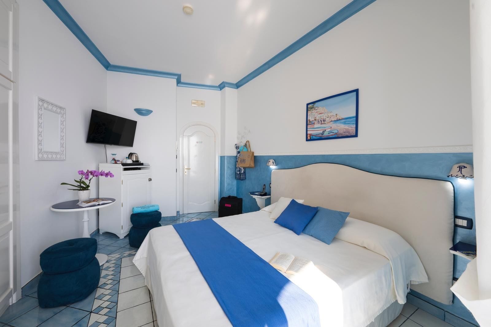 A hotel room with a large bed, a TV, a small table with a plant, and a painting on the wall.