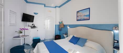 A hotel room with a large bed, a TV, a small table with a plant, and a painting on the wall.