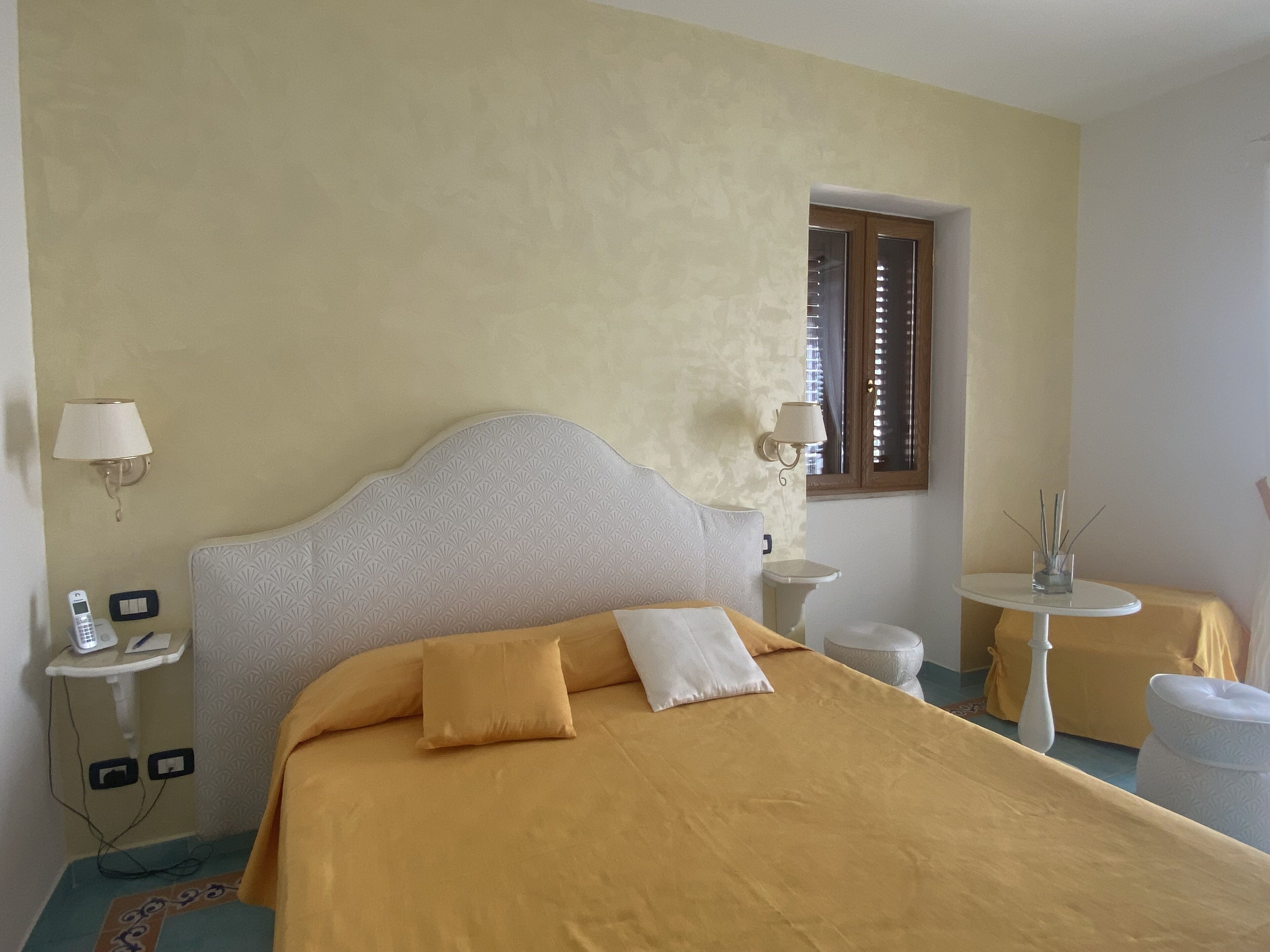 A hotel room with a large bed, a bedside table with a lamp, a small round table, and a window with blinds.