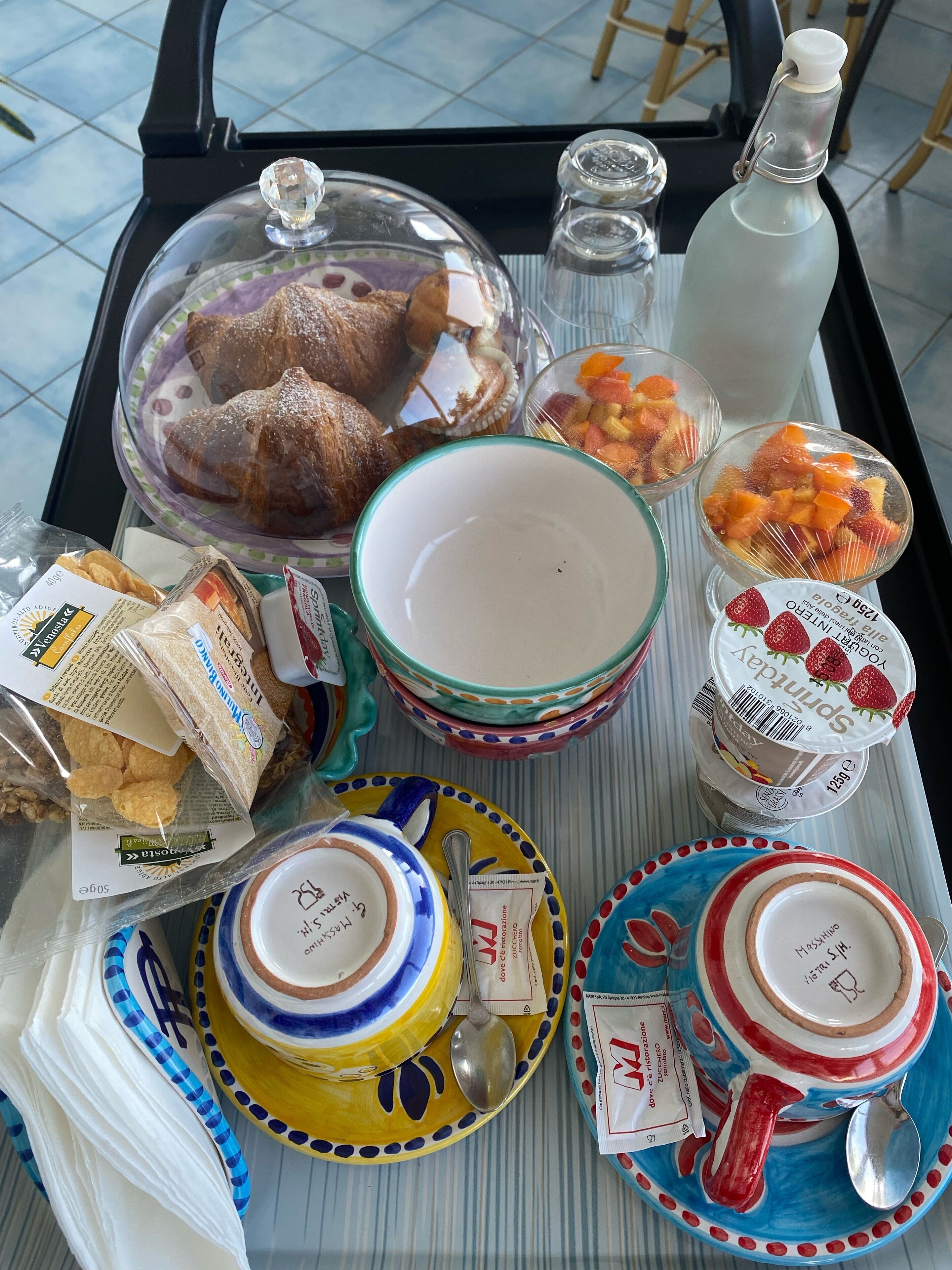 A tray with food items, including pastries, fruits, and condiments, along with colorful plates and a bottle.