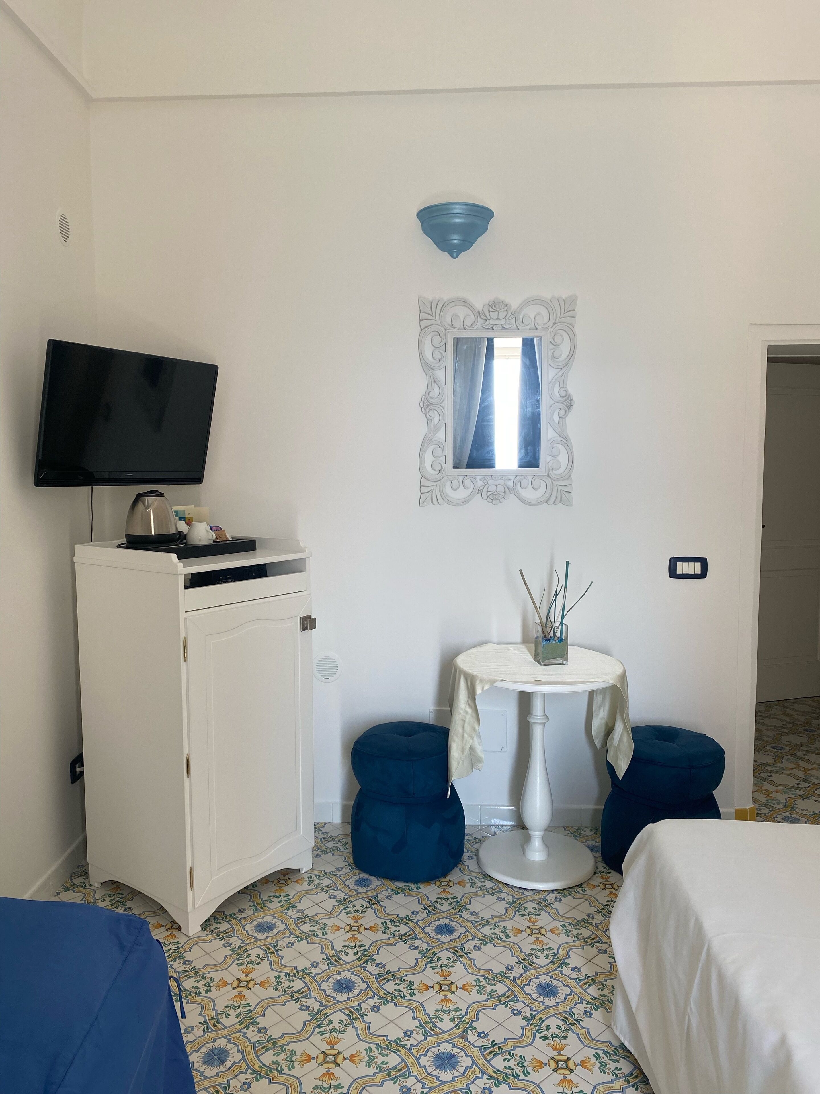 A hotel room with a television on a cabinet, a small round table with a mirror, and a bed with a white cover.