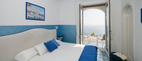 A hotel room with a large bed, a balcony with a view, and a painting on the wall.