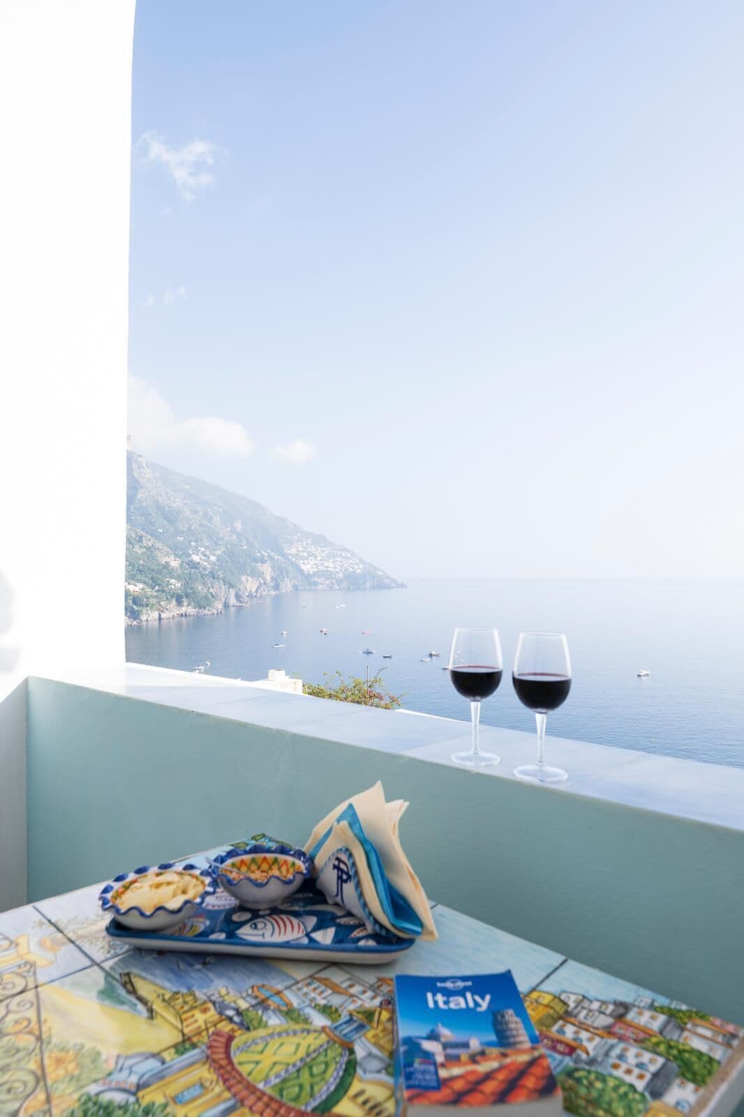 A table with a map, a book titled "Italy," and two glasses of red wine.