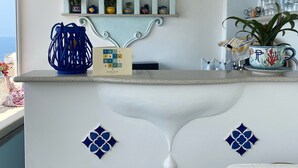 A kitchen with a white countertop, blue decorative tiles, a hanging light fixture, and a shelf with potted plants. - Palazzo Talamo (Positano)