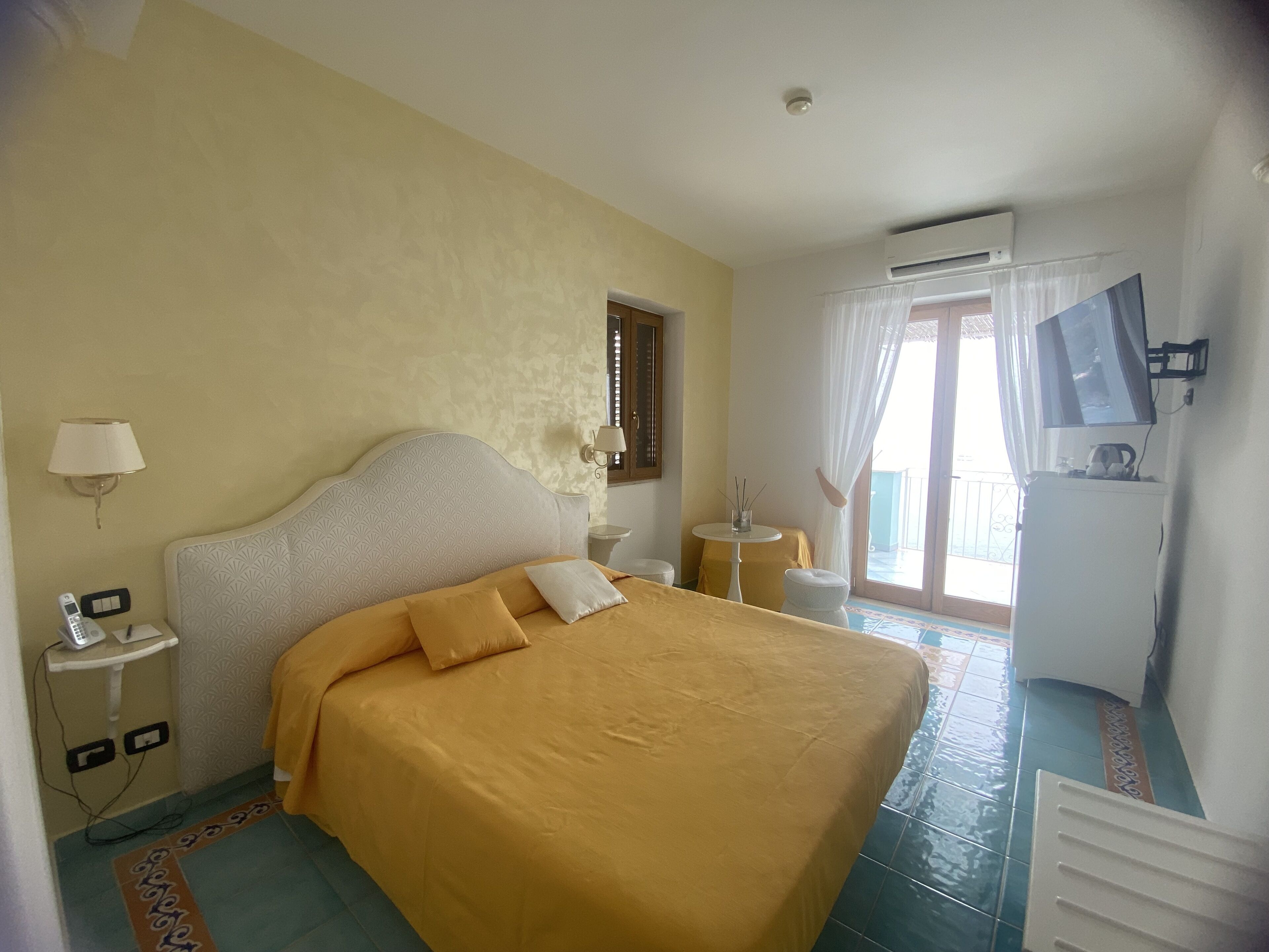 Habitación de hotel con cama, mesita de noche con lámpara, televisor y aire acondicionado.