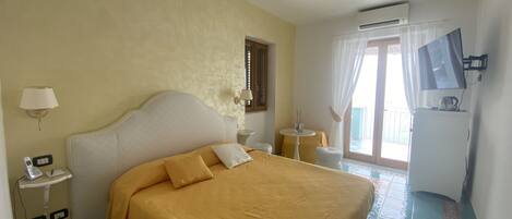 Habitación de hotel con cama, mesita de noche con lámpara, televisor y aire acondicionado.