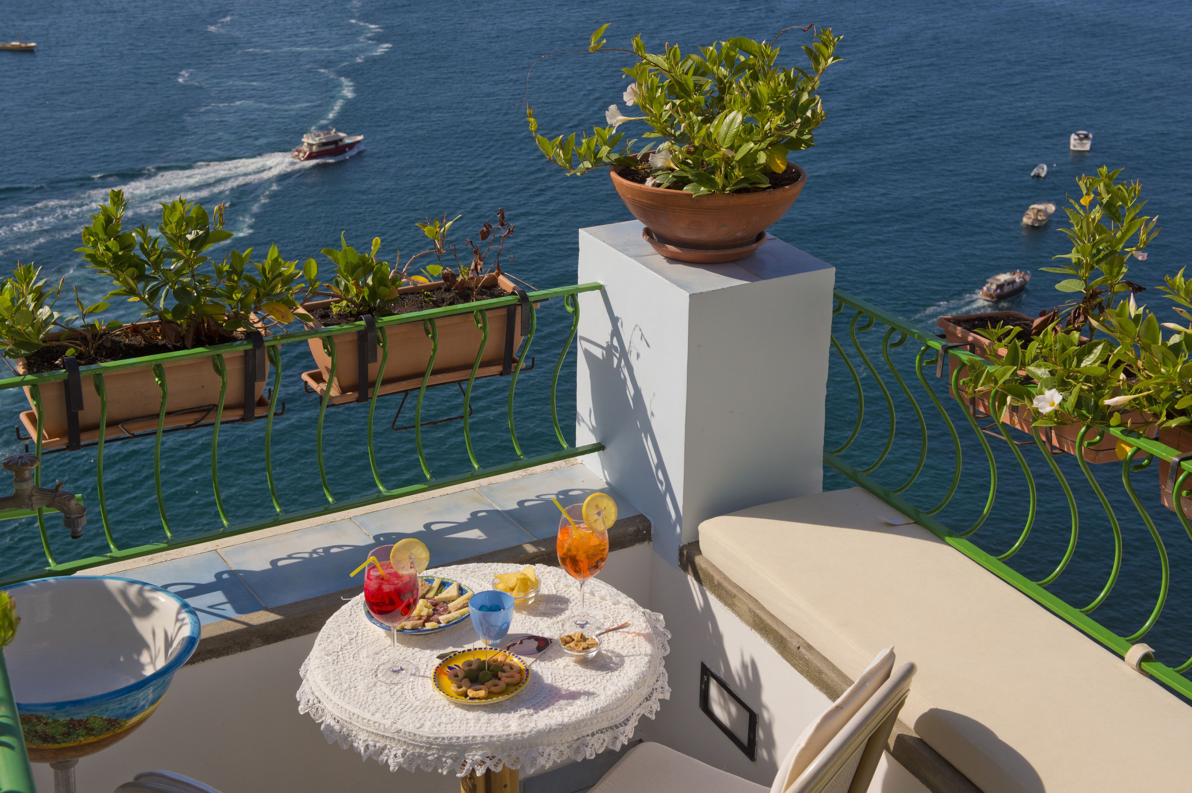 A balcony with a table set for dining, overlooking a body of water with boats.