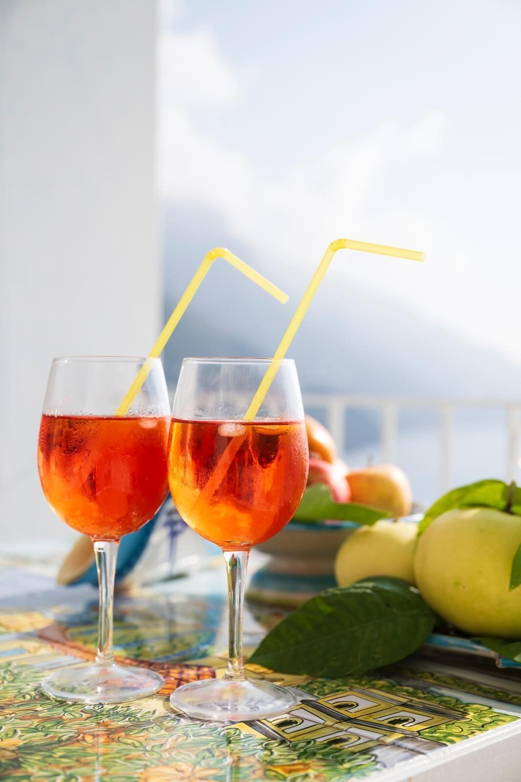 Two glasses of red beverage with yellow straws on a table with a colorful tablecloth.