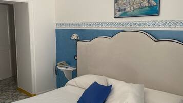 A bedroom with a bed, a nightstand, a telephone, and a painting of a coastal town on the wall.
