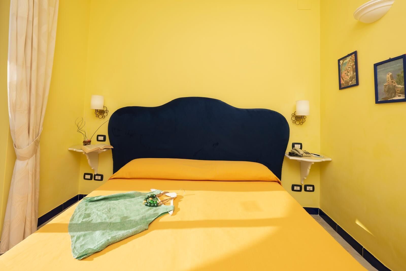 Una cama con cabecera oscura, paredes amarillas y dos mesitas de noche con lámparas.