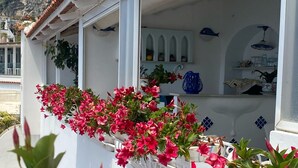A white building with a balcony adorned with pink flowers and blue fish-shaped decorations. - Palazzo Talamo (Positano)