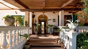 A covered outdoor area with steps leading to a door, surrounded by potted plants and a white balustrade. - Holiday House Le Palme (Amalfi)