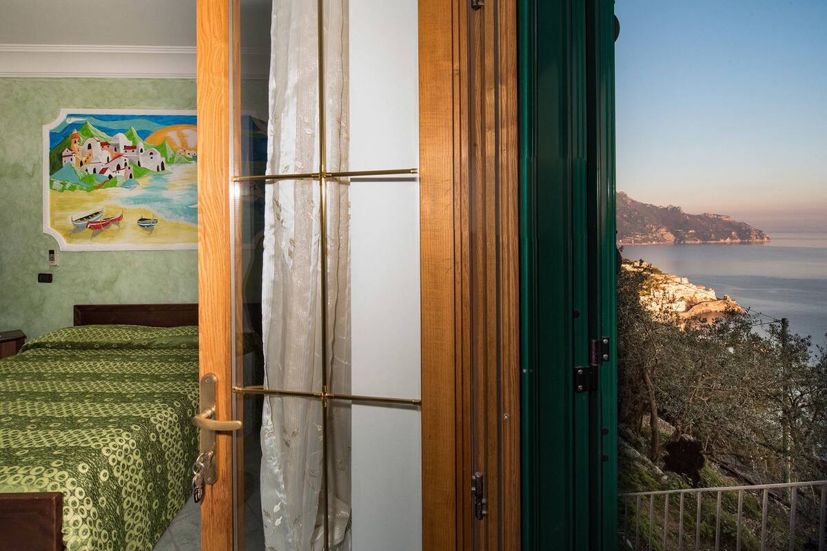 A room with a bed, a painting, and a view of the sea.