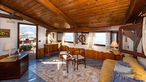 A cozy room with wooden beams, a wooden sofa, a table with chairs, and a view of the mountains through a window. - Holiday House Le Palme (Amalfi)
