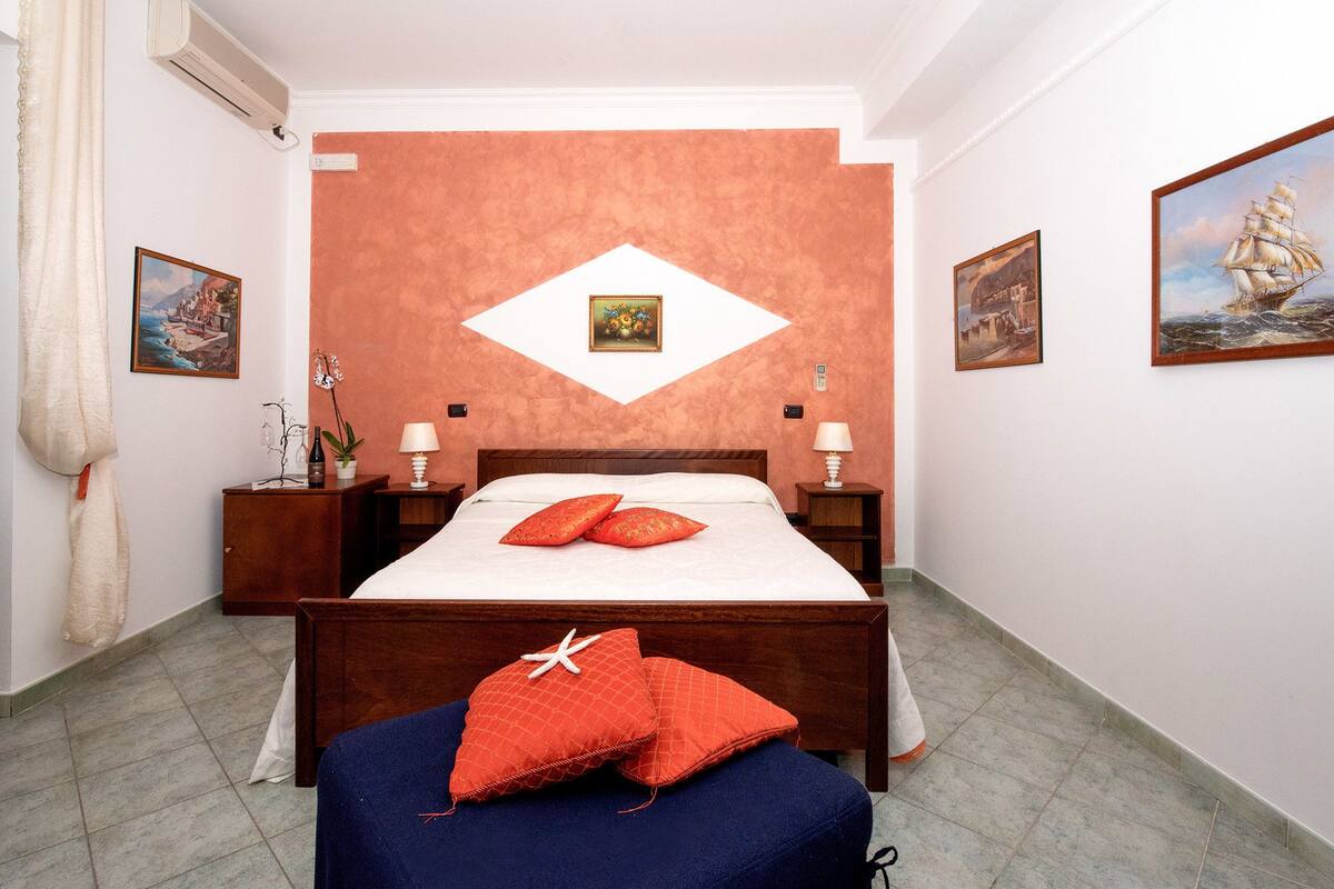 A hotel room with a bed, nightstands, a dresser, and a wall with paintings.