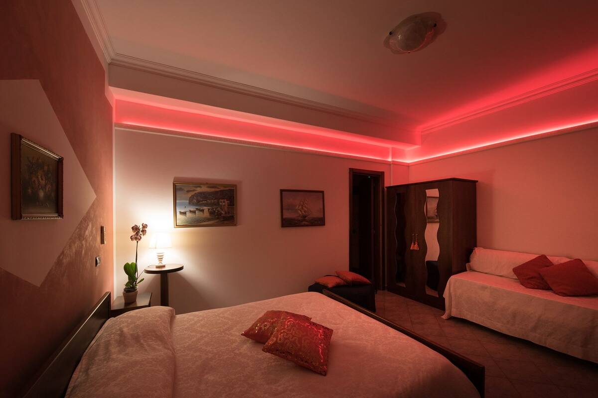 A hotel room with a bed, a bedside table with a lamp, and a mirror.