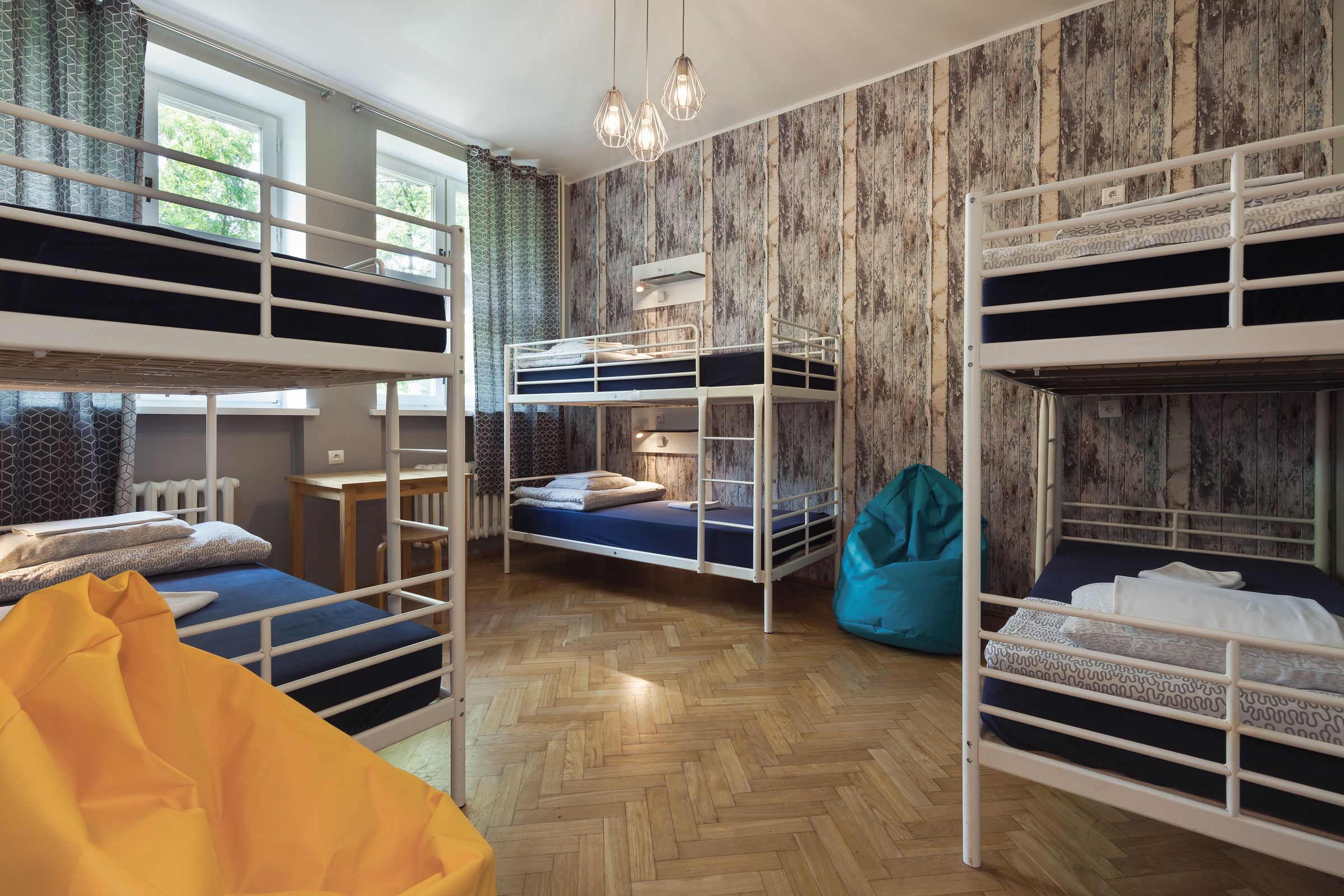 Un dormitorio con literas, piso de madera en espiga, una mesita pequeña y un sillón de peluche.