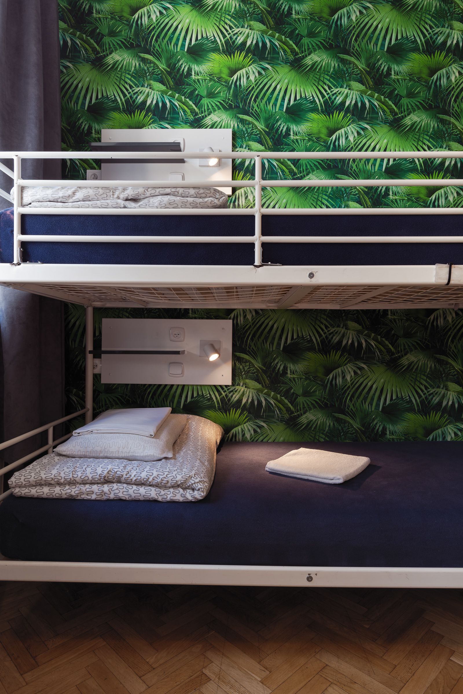 A bunk bed with a tropical leaf wallpaper, a white headboard, and a wooden floor.