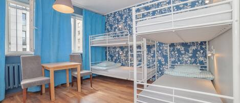 A bunk bed room with a wooden table and chairs, a window with blue curtains, and a patterned wall.