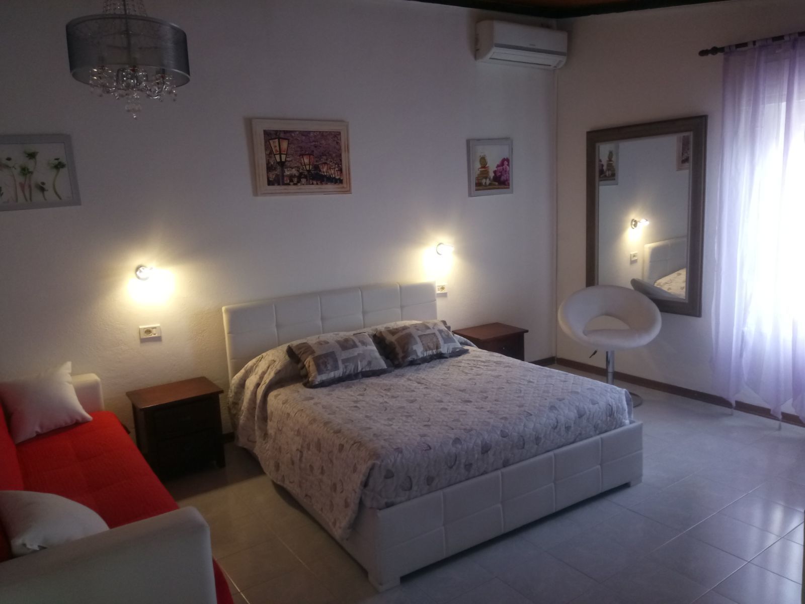 Un dormitorio con una cama grande, dos mesitas de noche, un sofá rojo, un espejo y luces empotradas en la pared.
