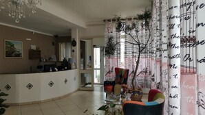 A reception area with a curved counter, a seating area with colorful chairs, and a decorative tree on the window. - Il Mirto e la Rosa Hoteles (Syracuse)