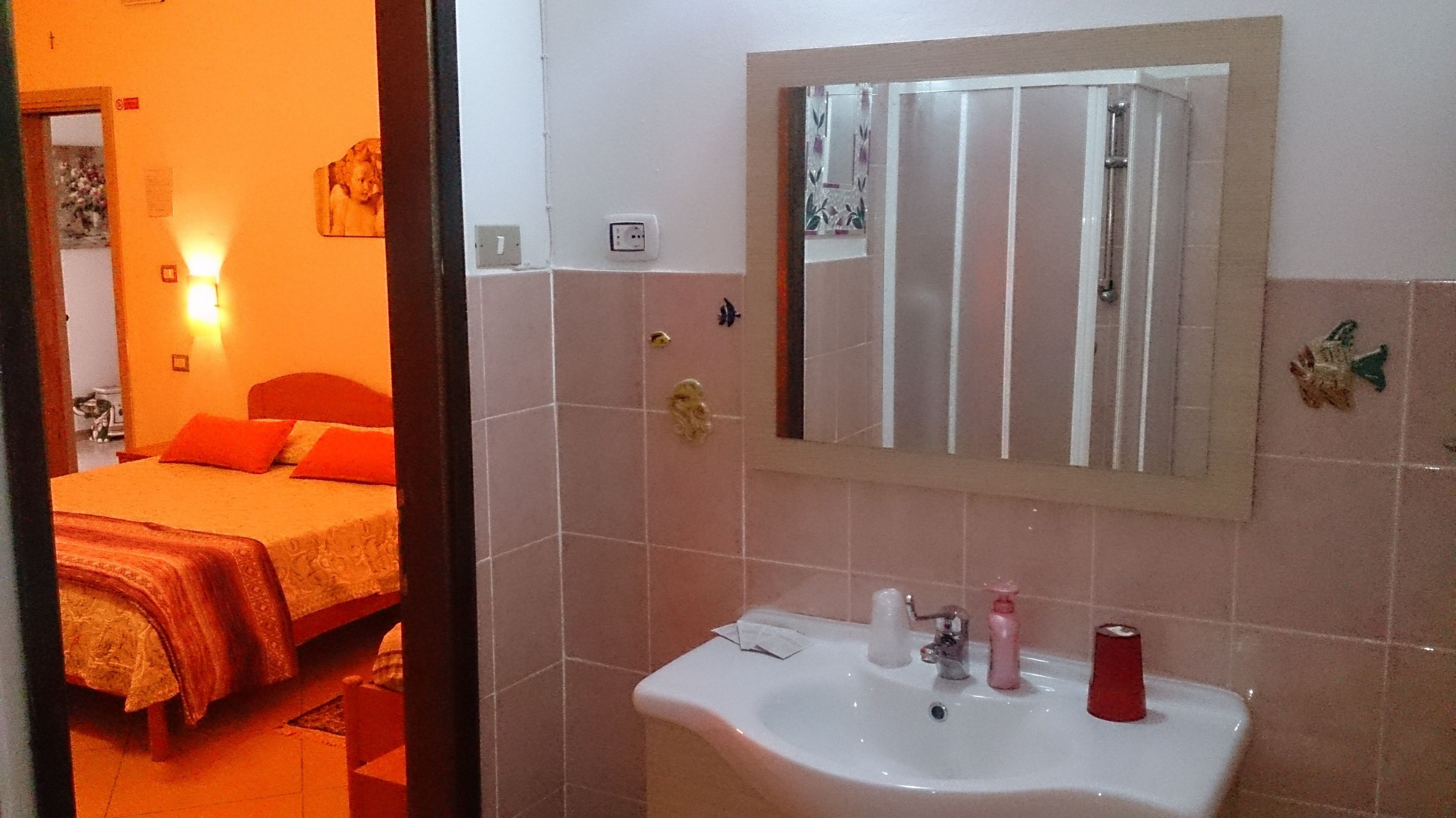 Ein Hotelzimmer mit Bett, Nachttischlampe, Spiegel und Waschbecken mit Toilettenartikeln.
