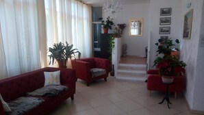 A living room with two red sofas, a chandelier, and several potted plants. - Il Mirto e la Rosa Hoteles (Syracuse)