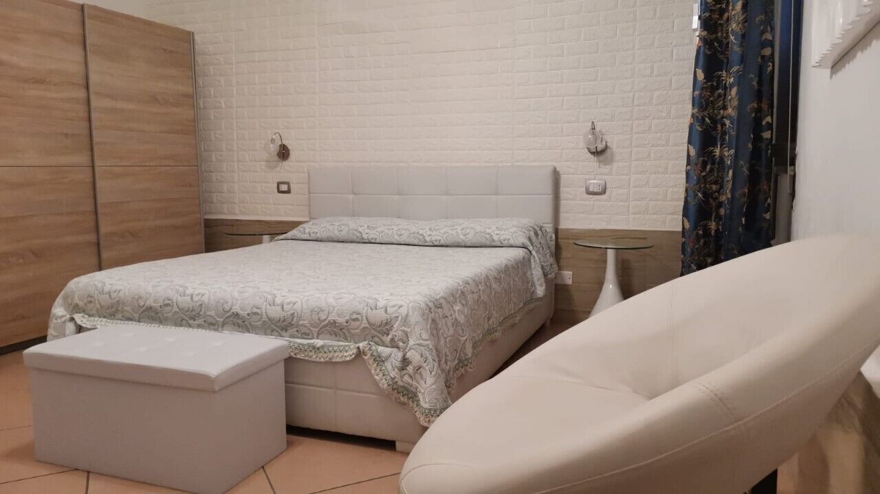 A bedroom with a bed, a nightstand, a chair, and a wardrobe.