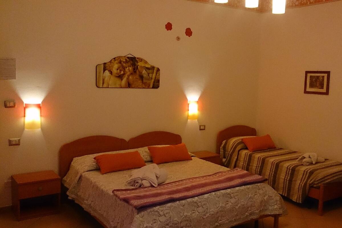 A hotel room with a large bed, two bedside tables, a wall-mounted lamp, and a framed picture.