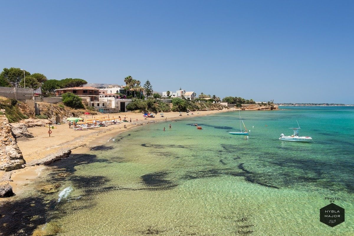 Ein Küstenstrand mit klarem türkisblauem Wasser, einem sandigen Ufer und einigen Booten.