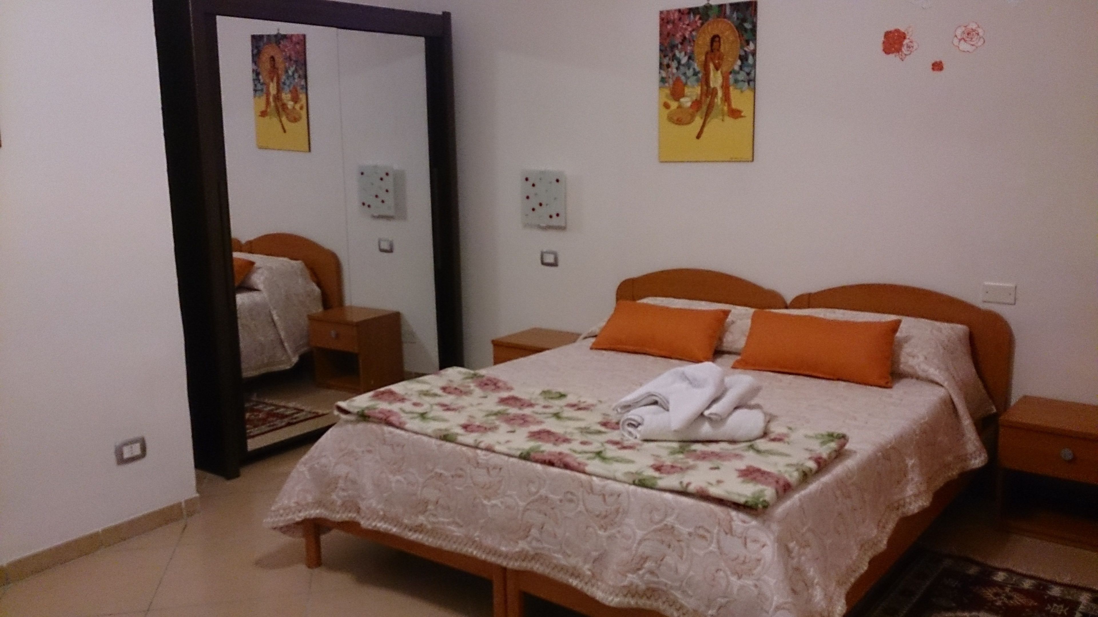 A bedroom with a bed, a nightstand, a mirror, and a wall with artwork.
