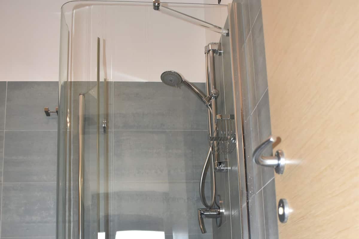 A glass-enclosed shower stall with a white towel on a stool, a handheld showerhead, and a wall-mounted faucet.