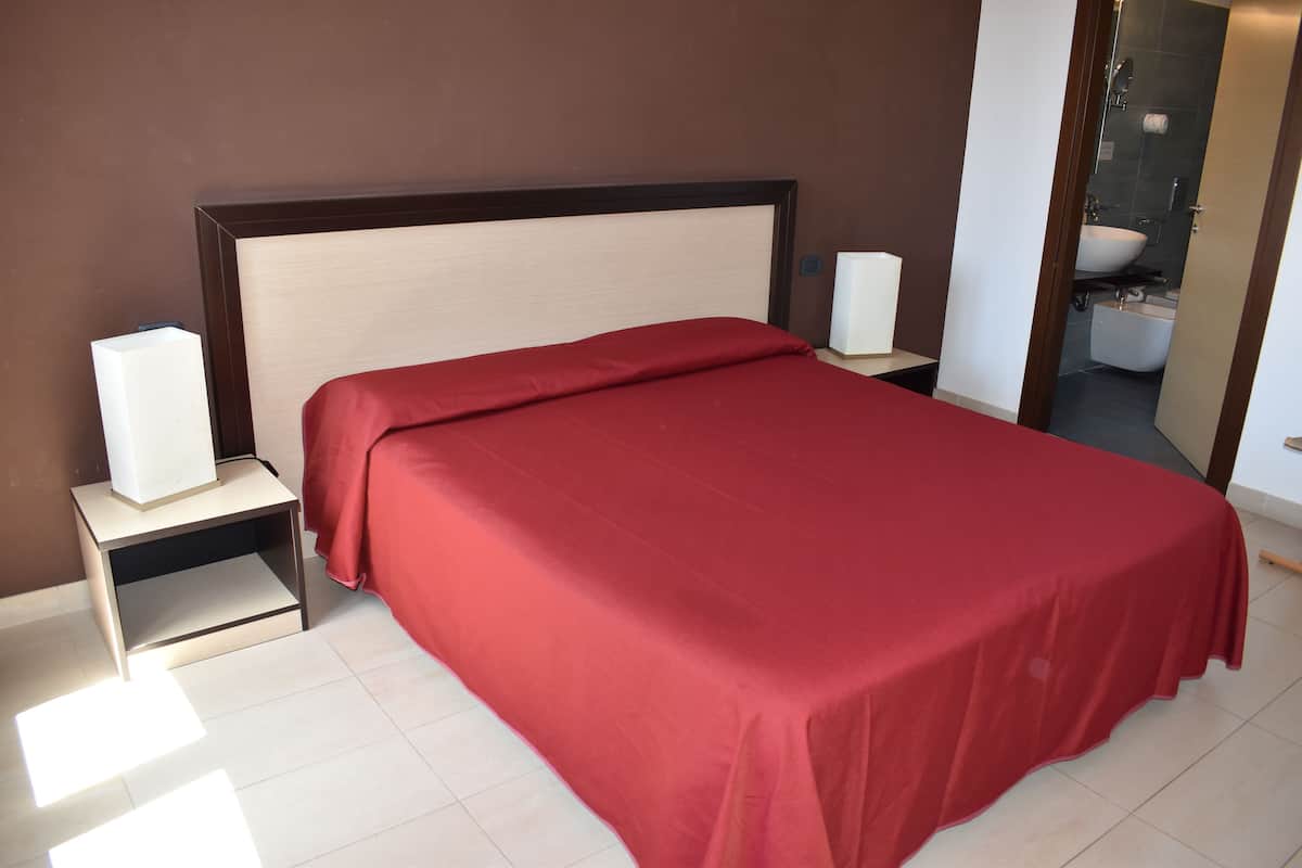 A neatly made bed with a red bedspread, two bedside tables with lamps, and a bathroom visible through an open door.
