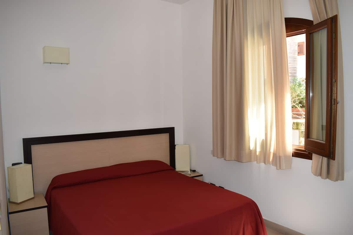 A hotel room with a bed, bedside lamps, a window with curtains, and a wall-mounted light fixture.
