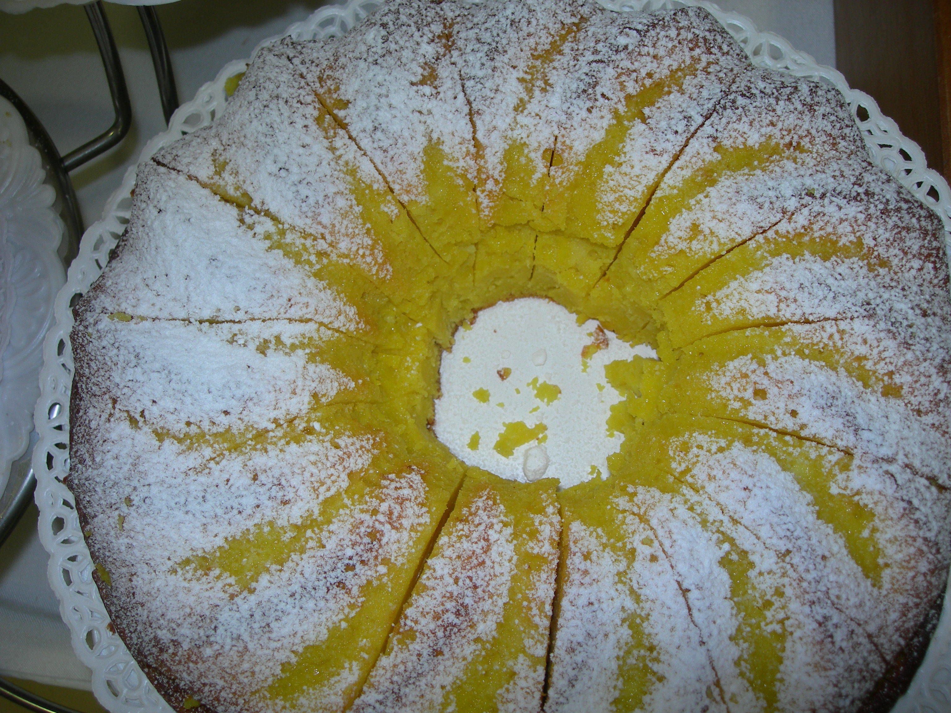 A round cake with white frosting and yellow filling, dusted with powdered sugar.