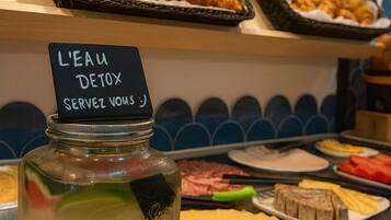 Un buffet proposant divers plats, notamment des croissants et un bocal étiqueté « EAU DÉTOX ».