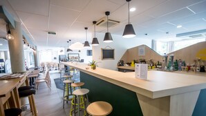 Zona de bar moderna con taburetes altos, iluminación colgante y una barra con varias botellas y un menú en la pizarra.