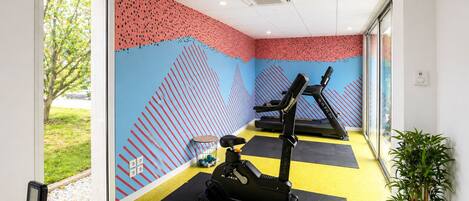 Un gimnasio con equipo de ejercicio, suelo amarillo y pared con diseño.