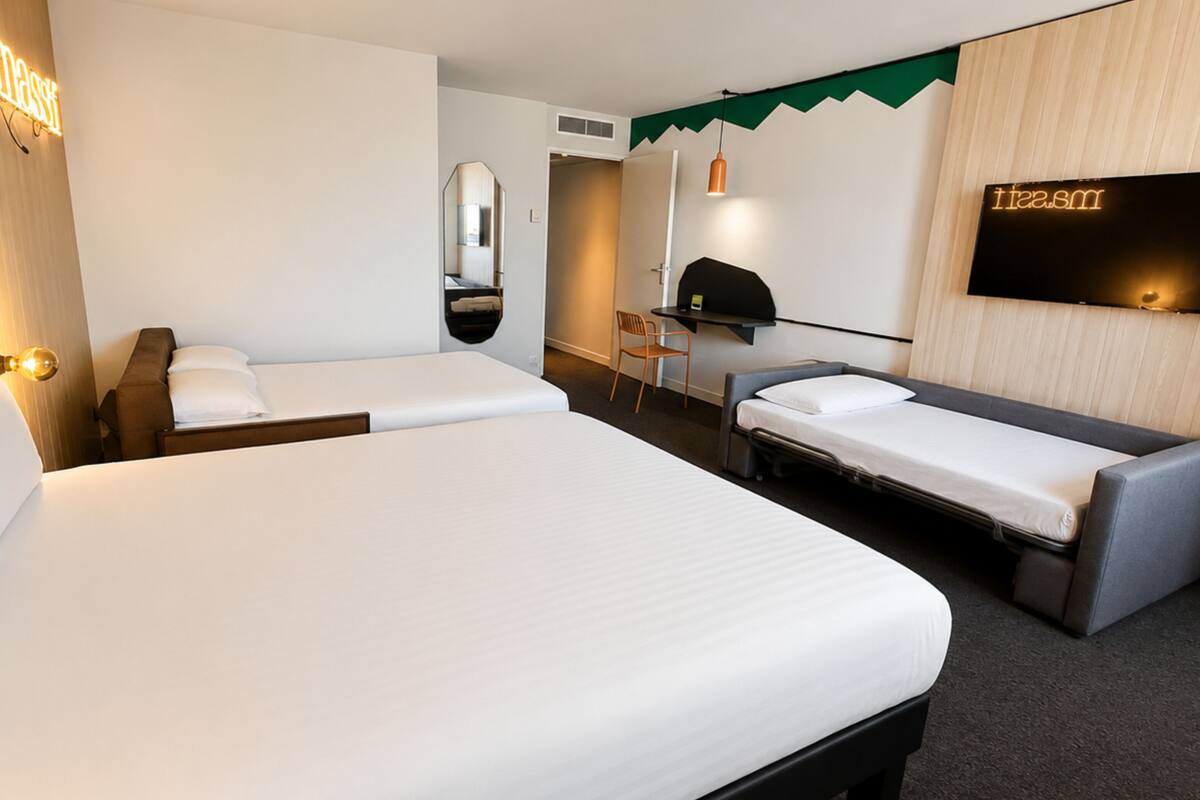 Habitación de hotel con dos camas, un escritorio, una silla, un televisor y un espejo.