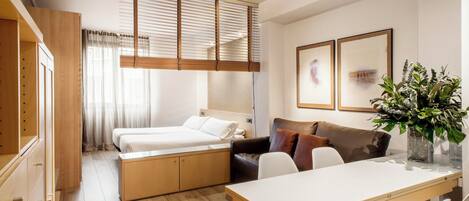A compact hotel room with a bed, a sofa, a dining table, and a small kitchen area.