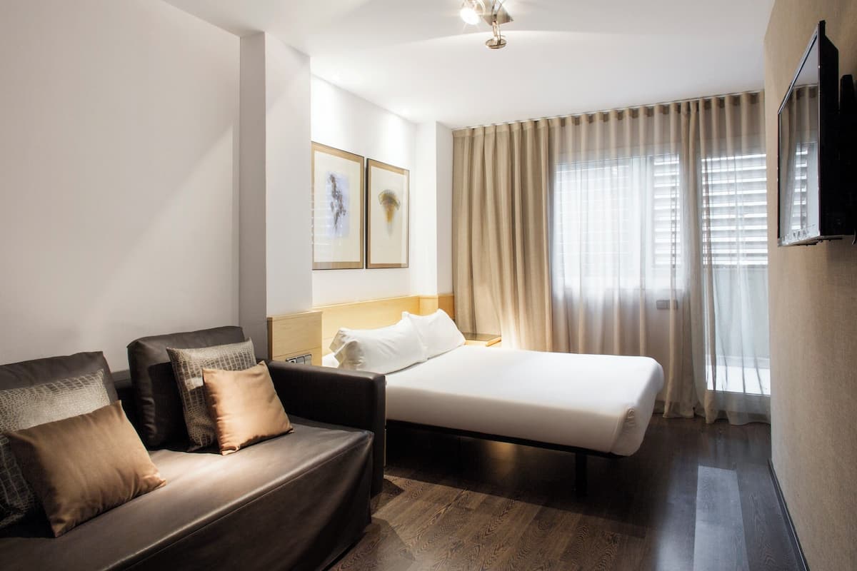 A hotel room with a bed, a sofa, and a TV.