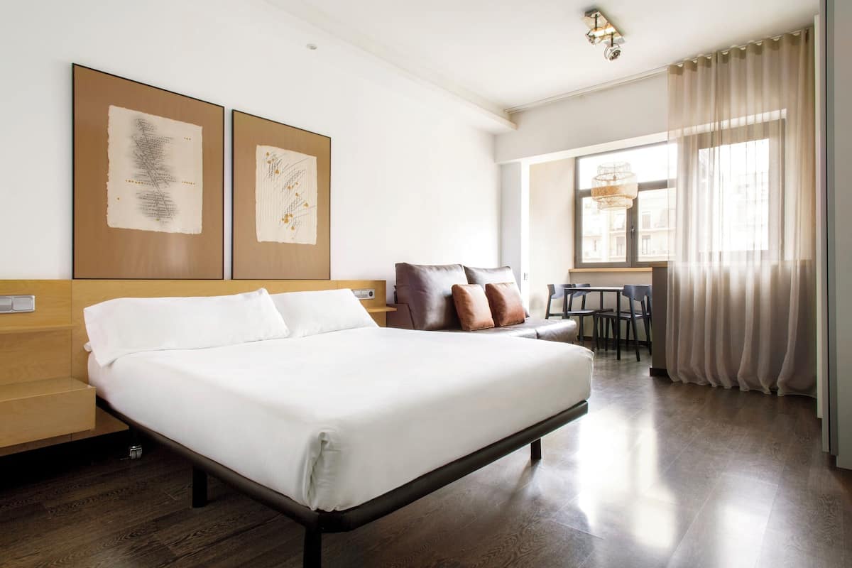 A hotel room with a large bed, a desk, and two framed artworks on the wall.